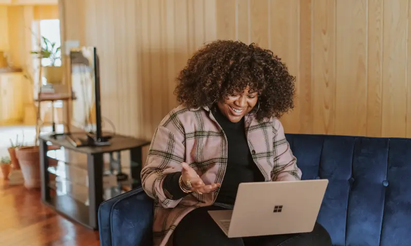 A person sitting on a couch partaking in a video call from their laptop